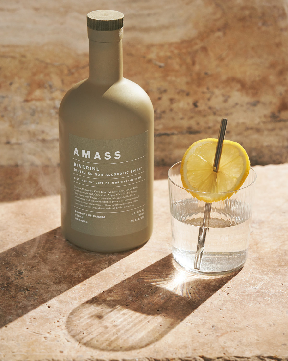 Riverine bottle next to a cocktail glass with lemon and straw